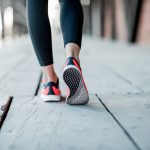 Sports woman in running shoes standing back on the wooden floor, close-up view focused on the sneakers